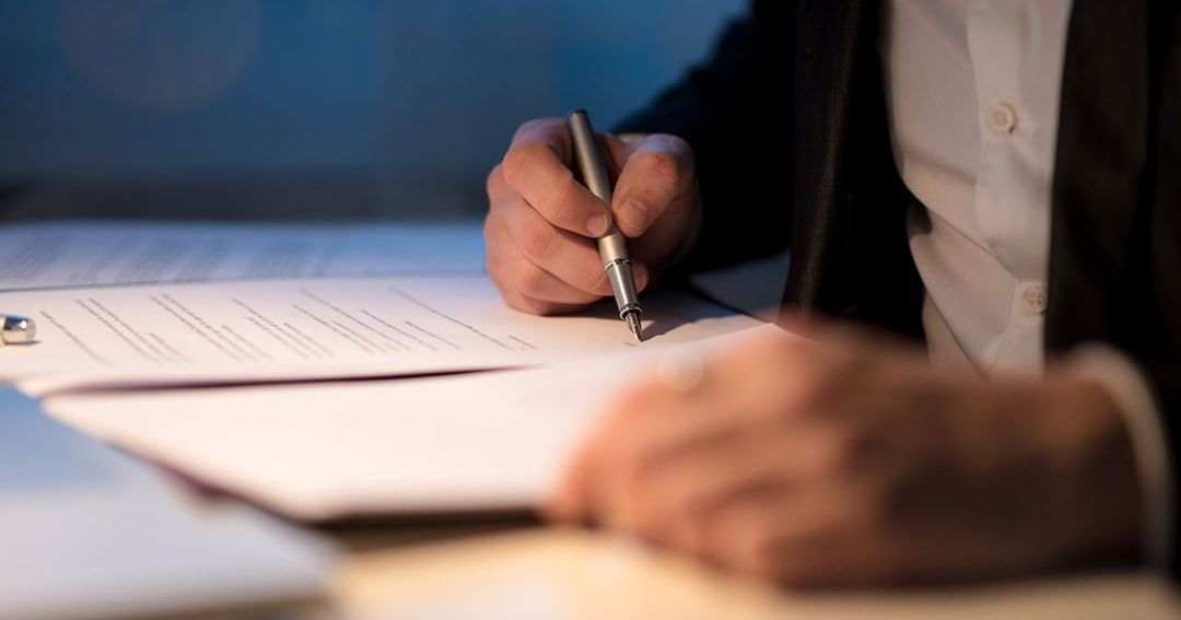 A man is writing on a piece of paper with a pen.