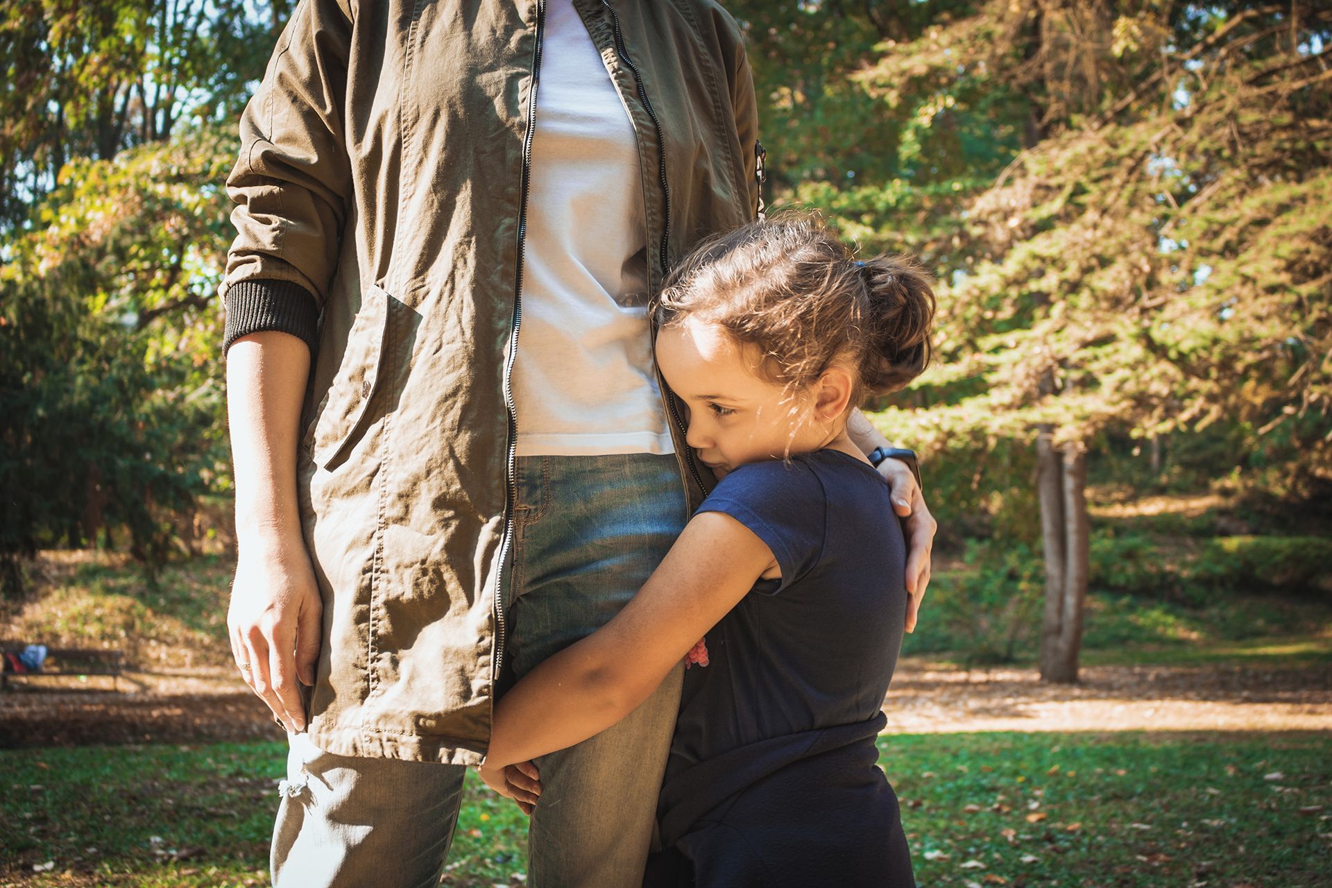 A woman is hugging a little girl in a park.