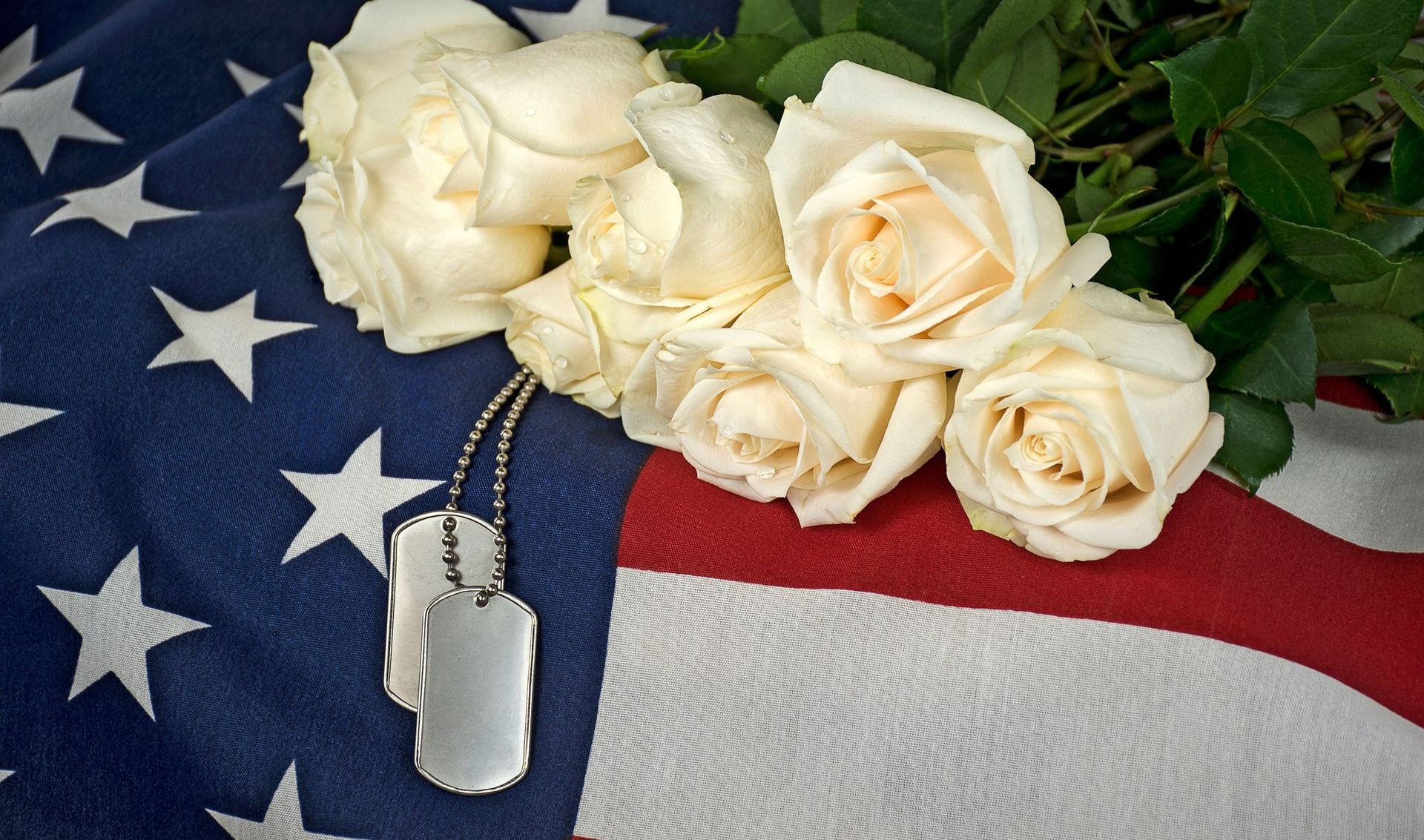 A flag with white roses and dog tags on it