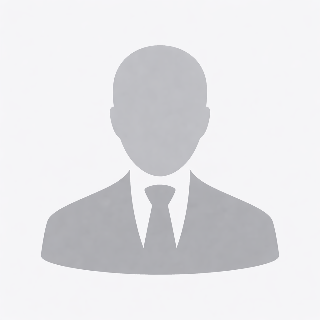 Football coach with arms crossed, standing on a football field. He wears a navy polo shirt and gray pants.