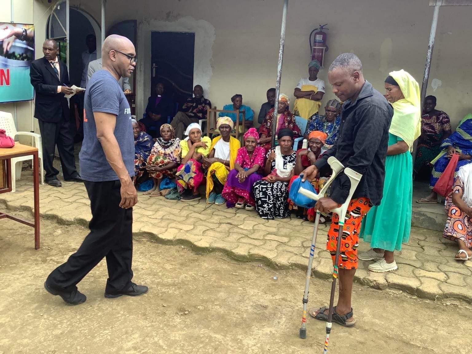 A man with crutches is standing in front of a group of people.