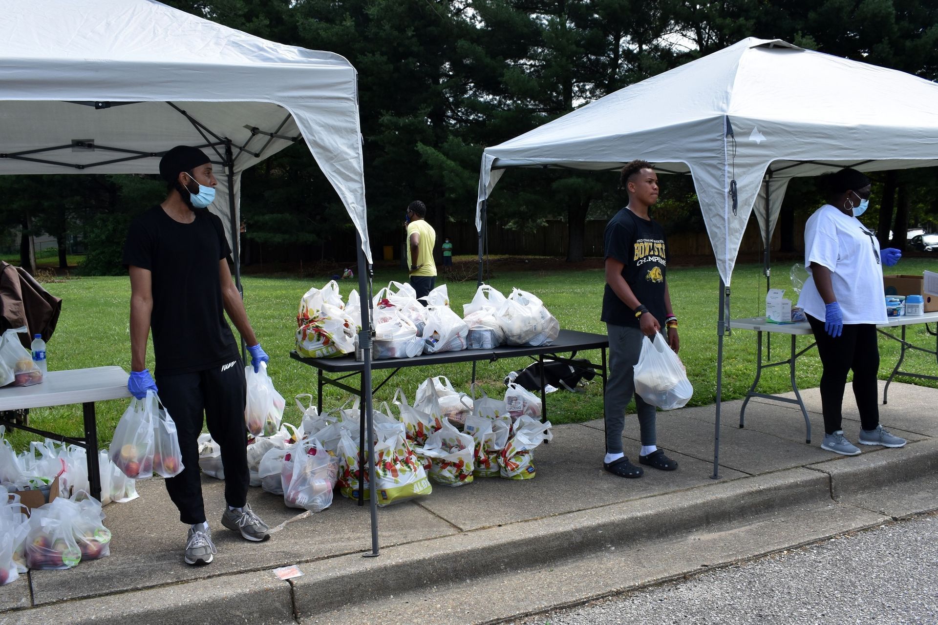 A group of people are standing under tents holding bags of food.