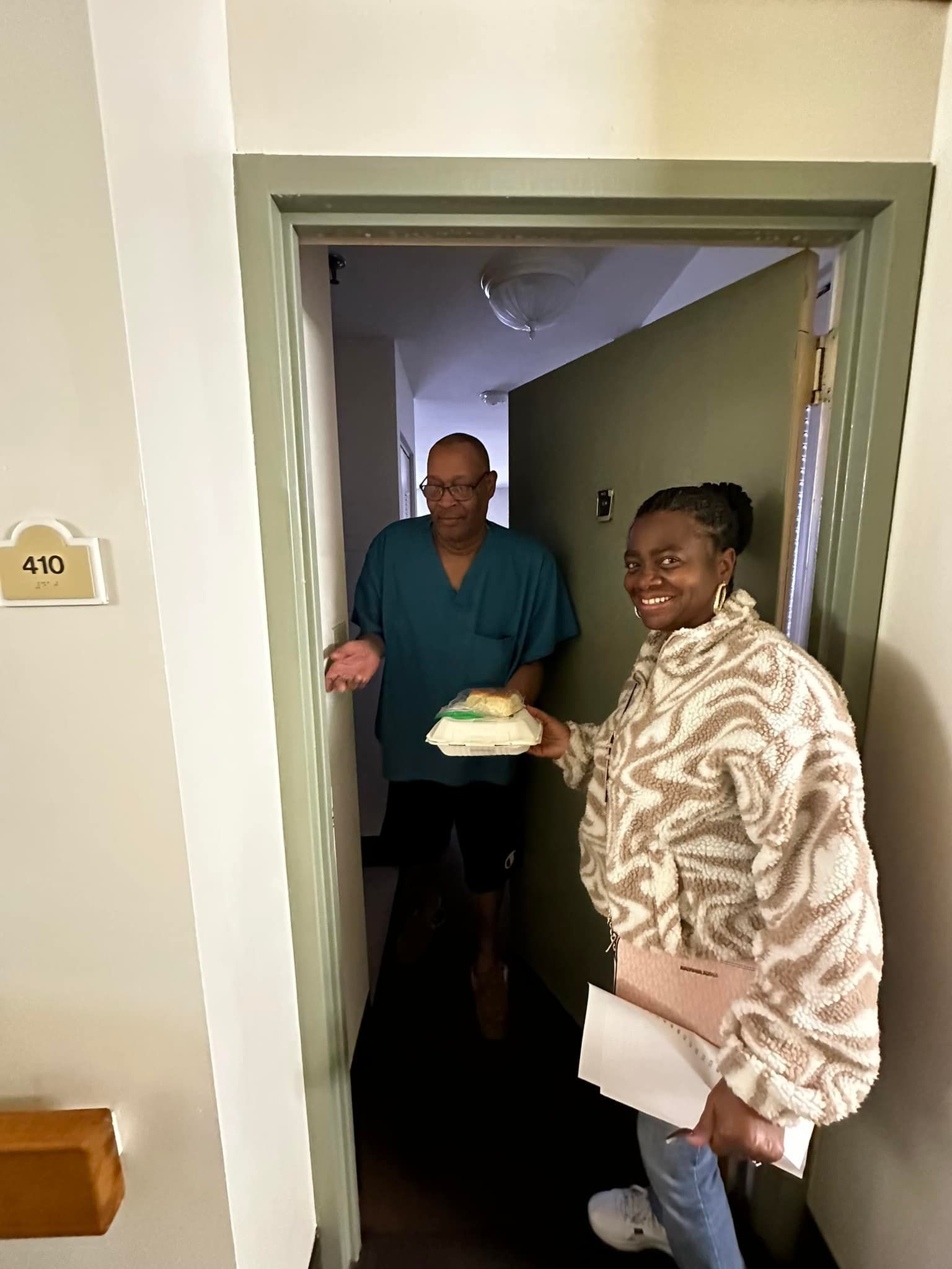 A man and a woman are standing in a hallway holding a cake.