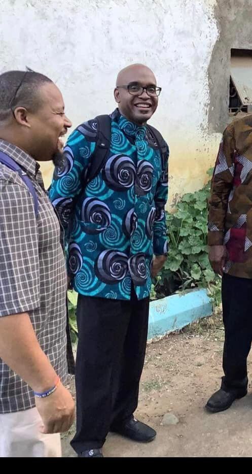 A man in a blue shirt is standing next to two other men.