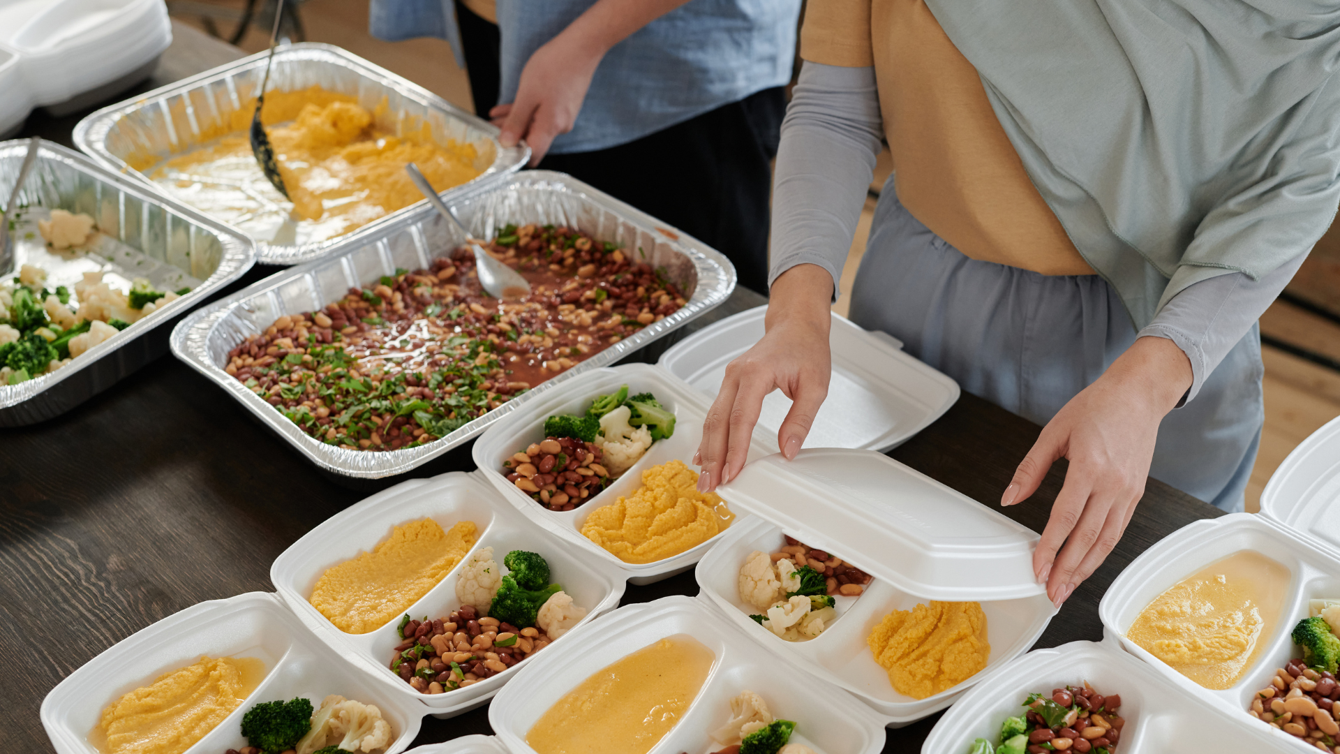 A woman is taking a container of food from a table.