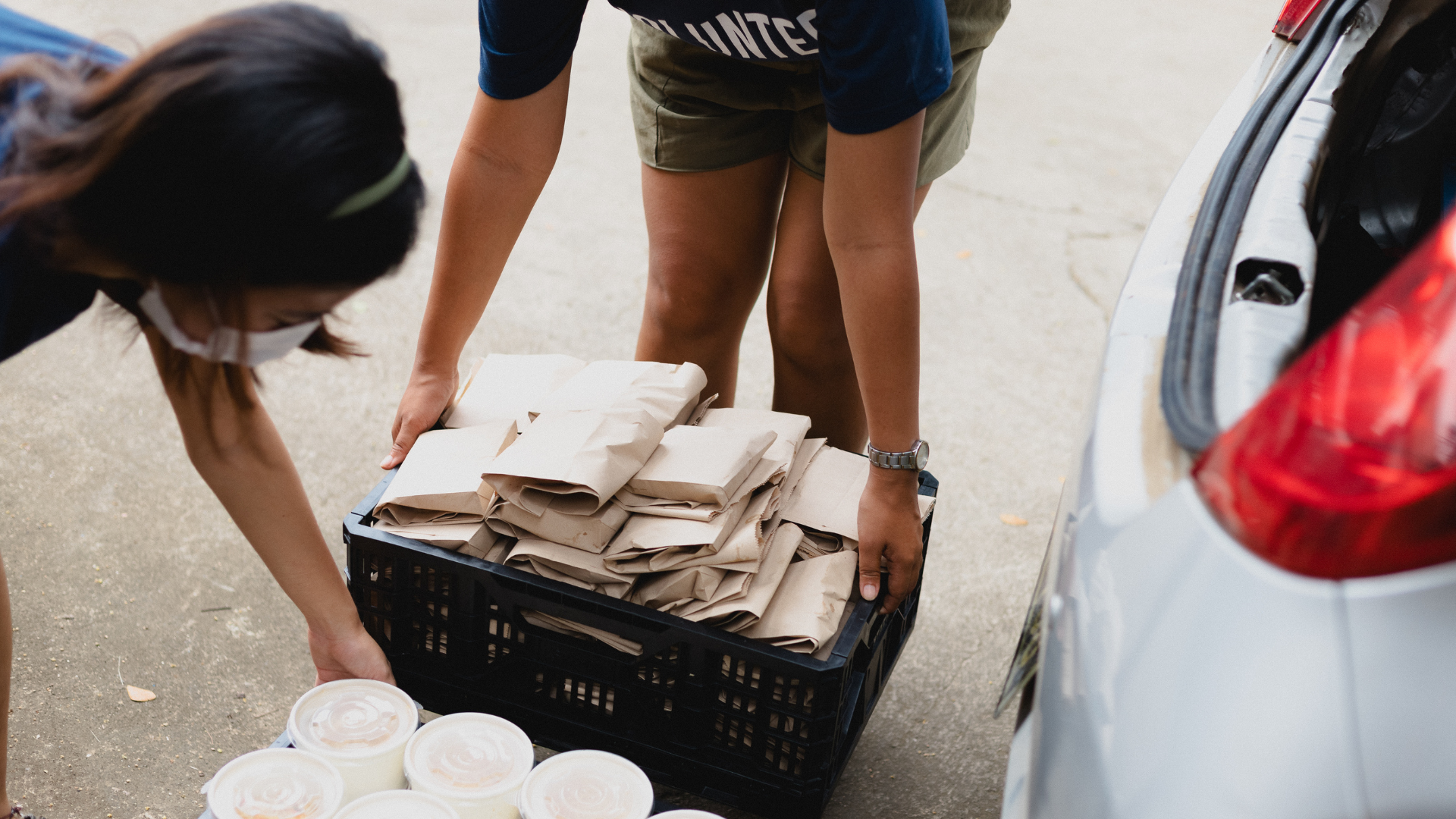 Two women are loading a crate of food into a car.