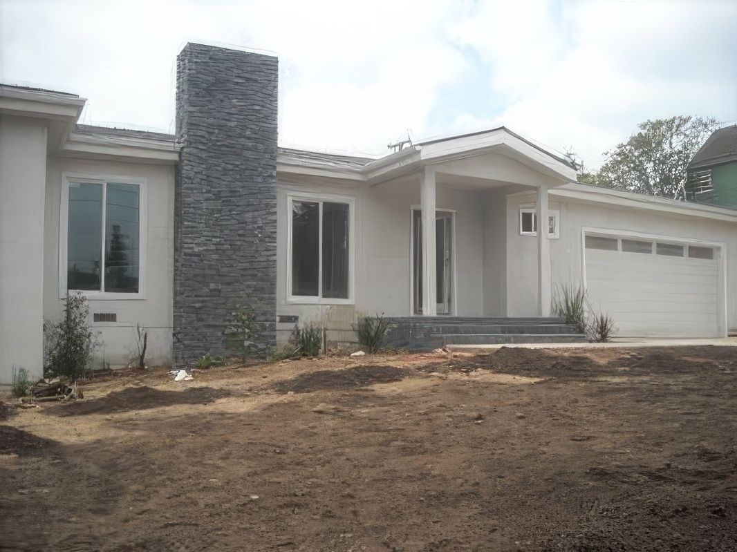 A white house with a stone chimney is sitting on top of a dirt field.