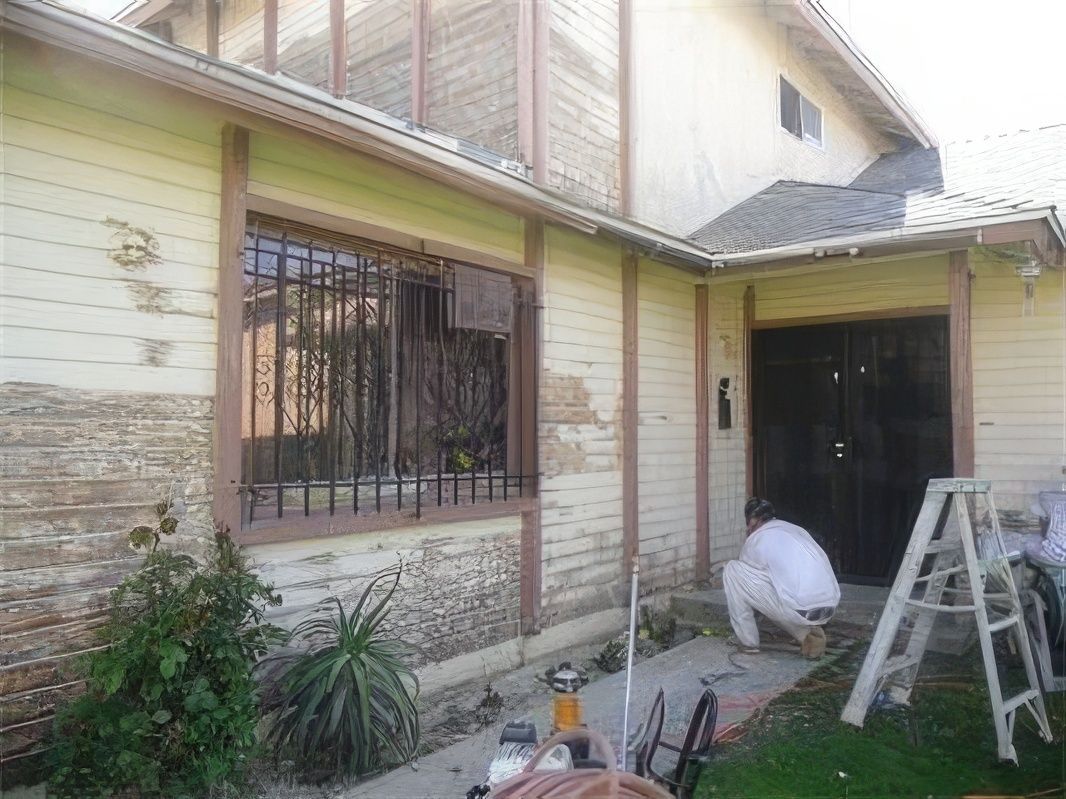 A man is kneeling down in front of a house being painted.