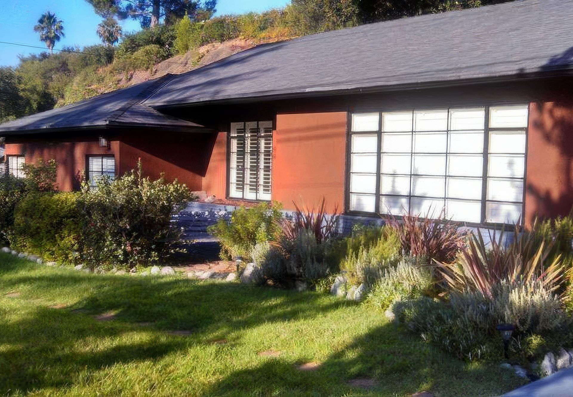 A house with a lot of windows is surrounded by grass and bushes