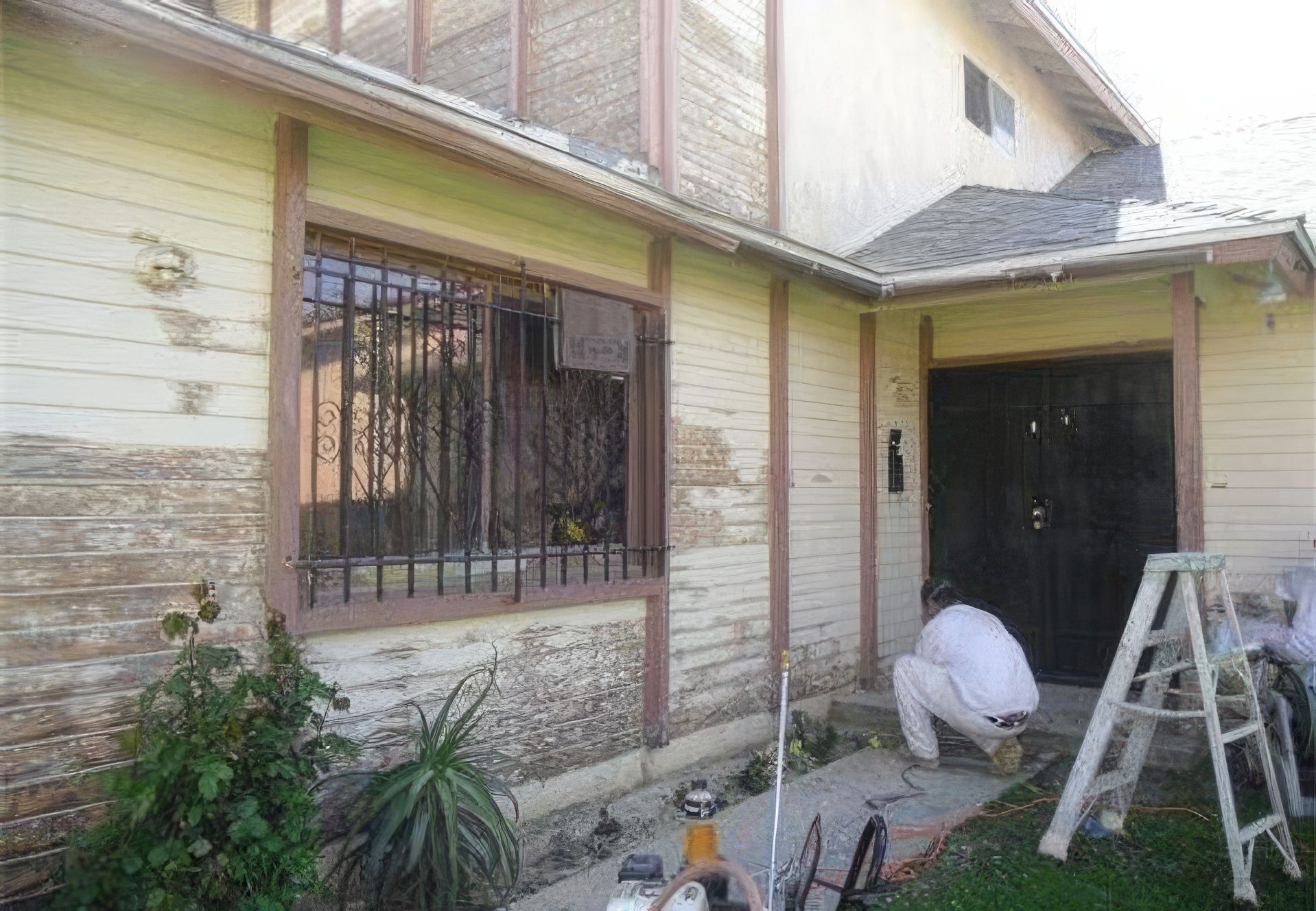 A man is kneeling in front of a house that is being painted.