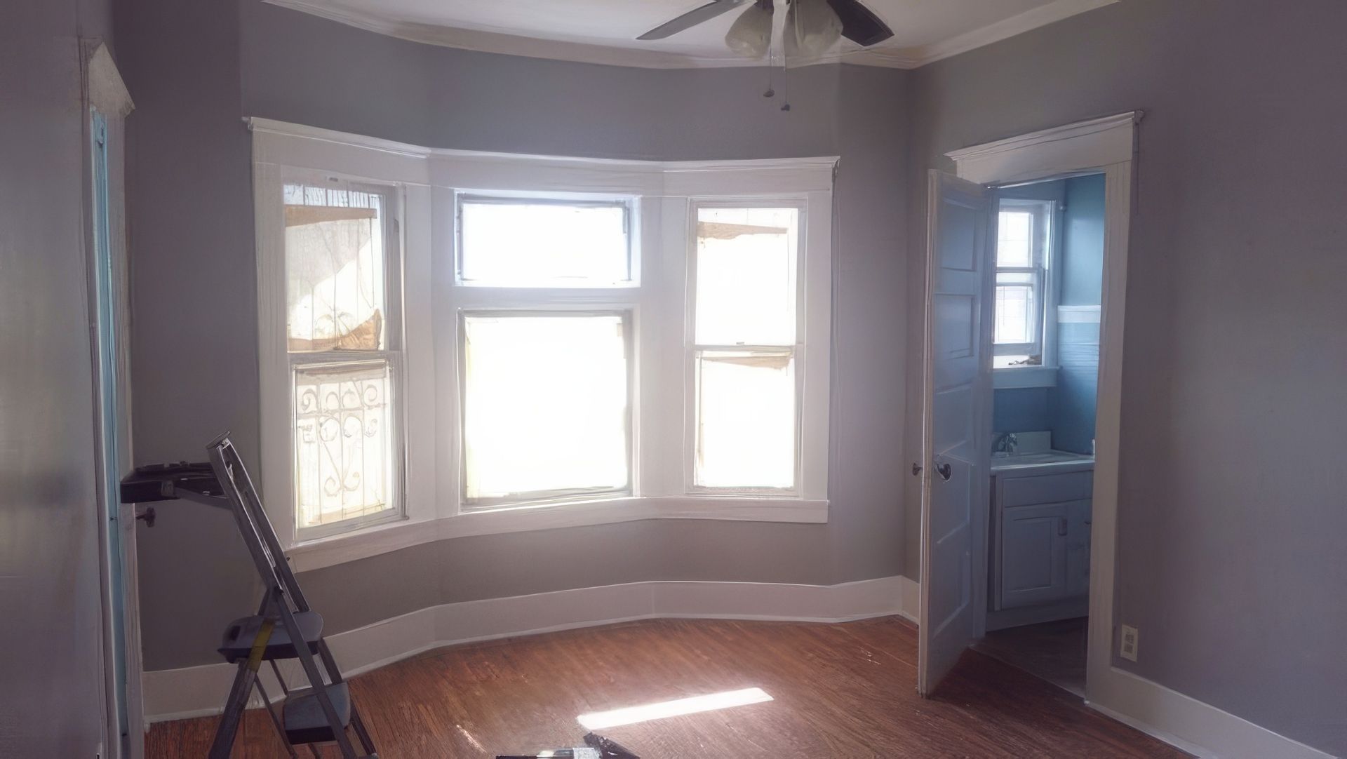 An empty room with a large bay window and a ceiling fan.