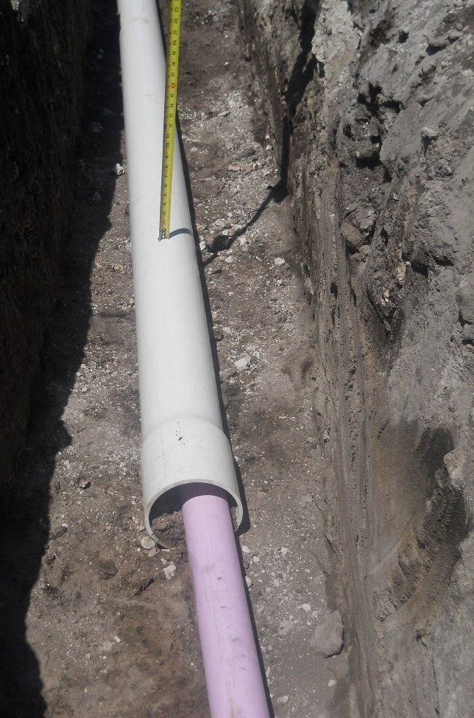 A white pipe is laying in the dirt next to a pink pipe
