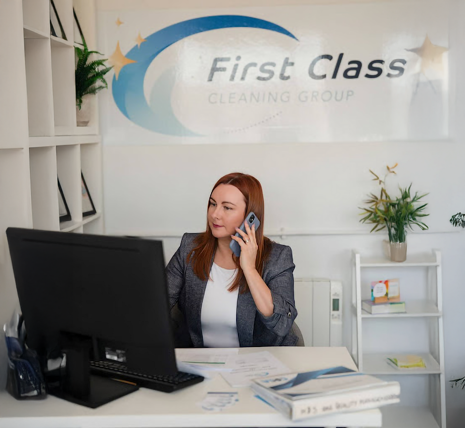 A woman in a blazer talks on the phone at a desk in an office.  The 