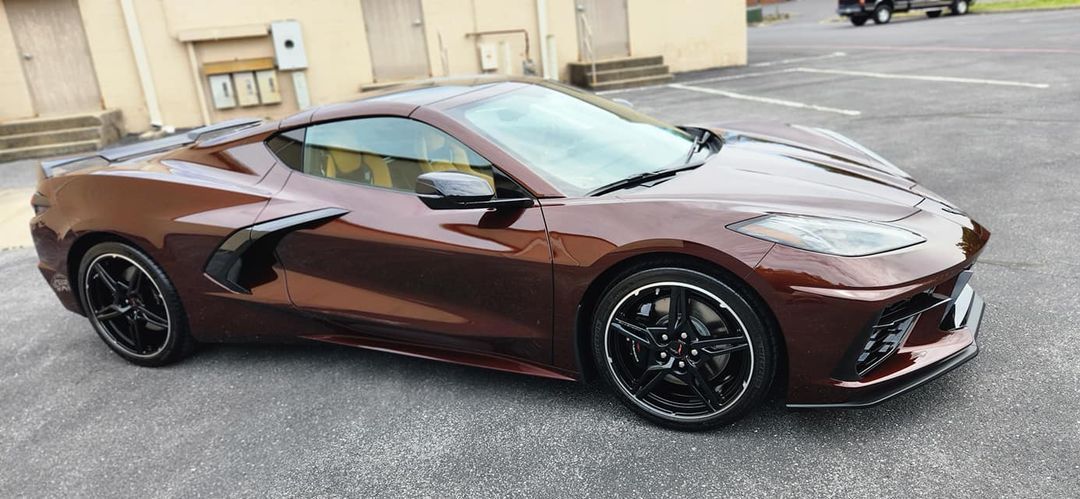 A brown sports car is parked in a parking lot in front of a building.