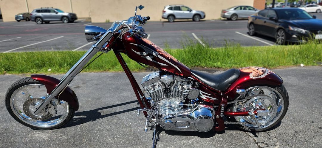 A red chopper motorcycle is parked in a parking lot.