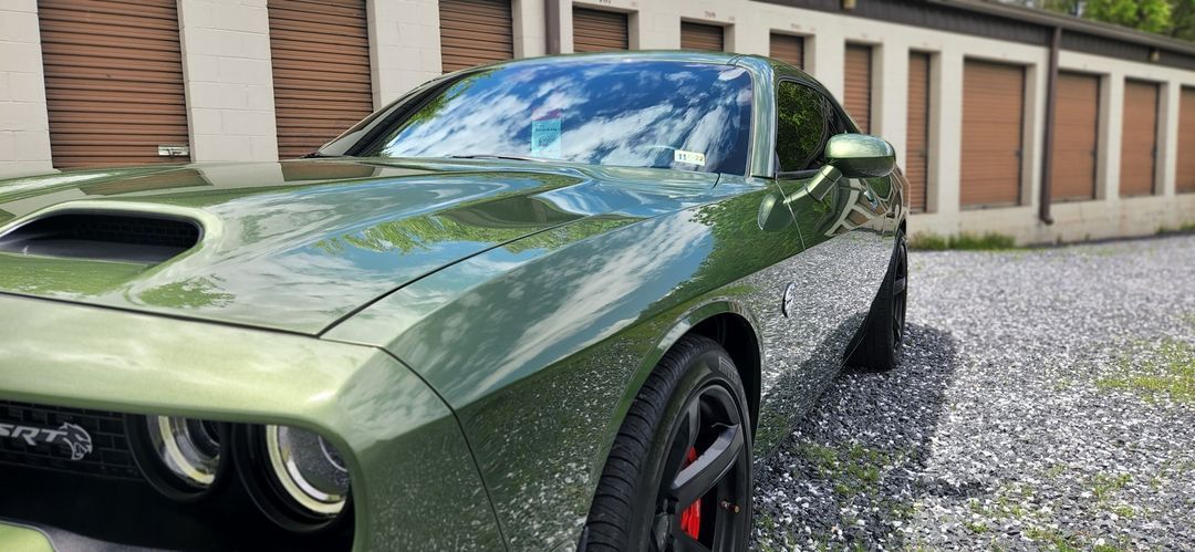 A green dodge challenger is parked in front of a building.