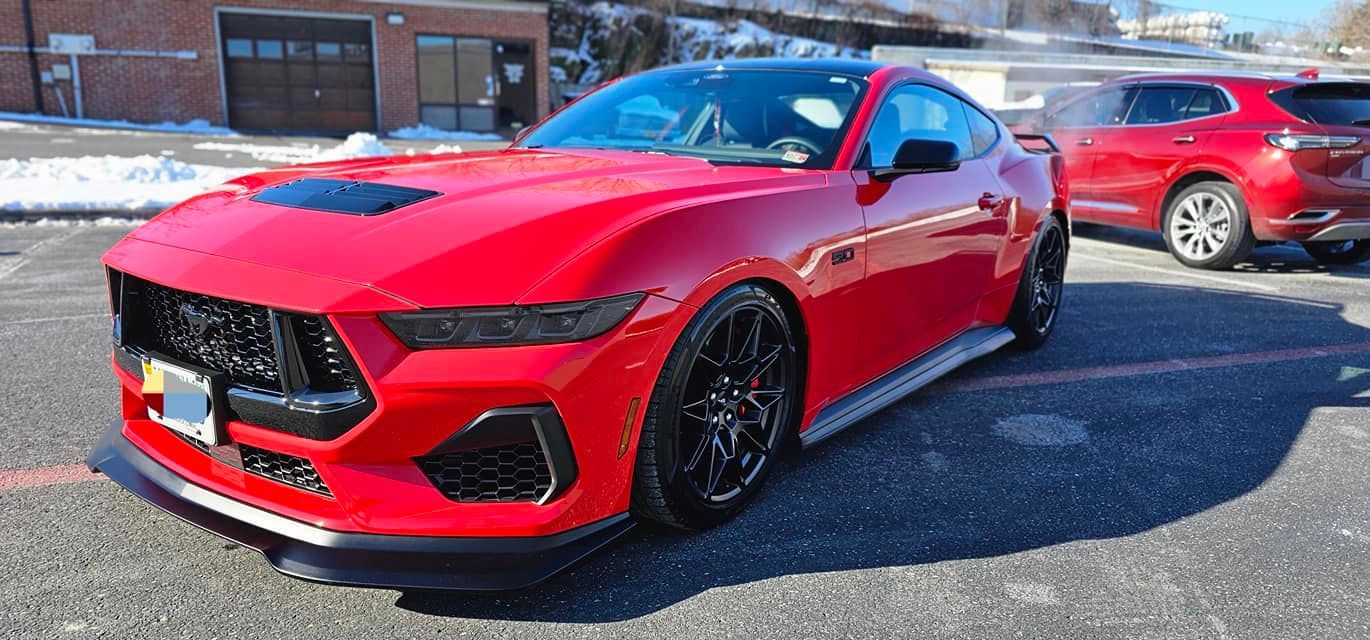 A red mustang is parked in a parking lot next to another red car.