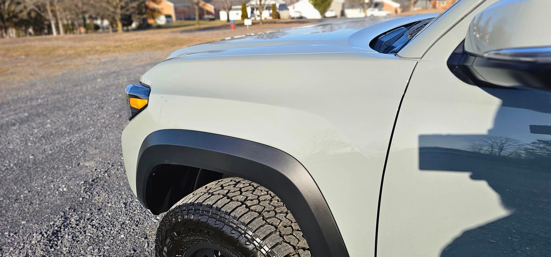 A white truck with black fender flares is parked on a gravel road.