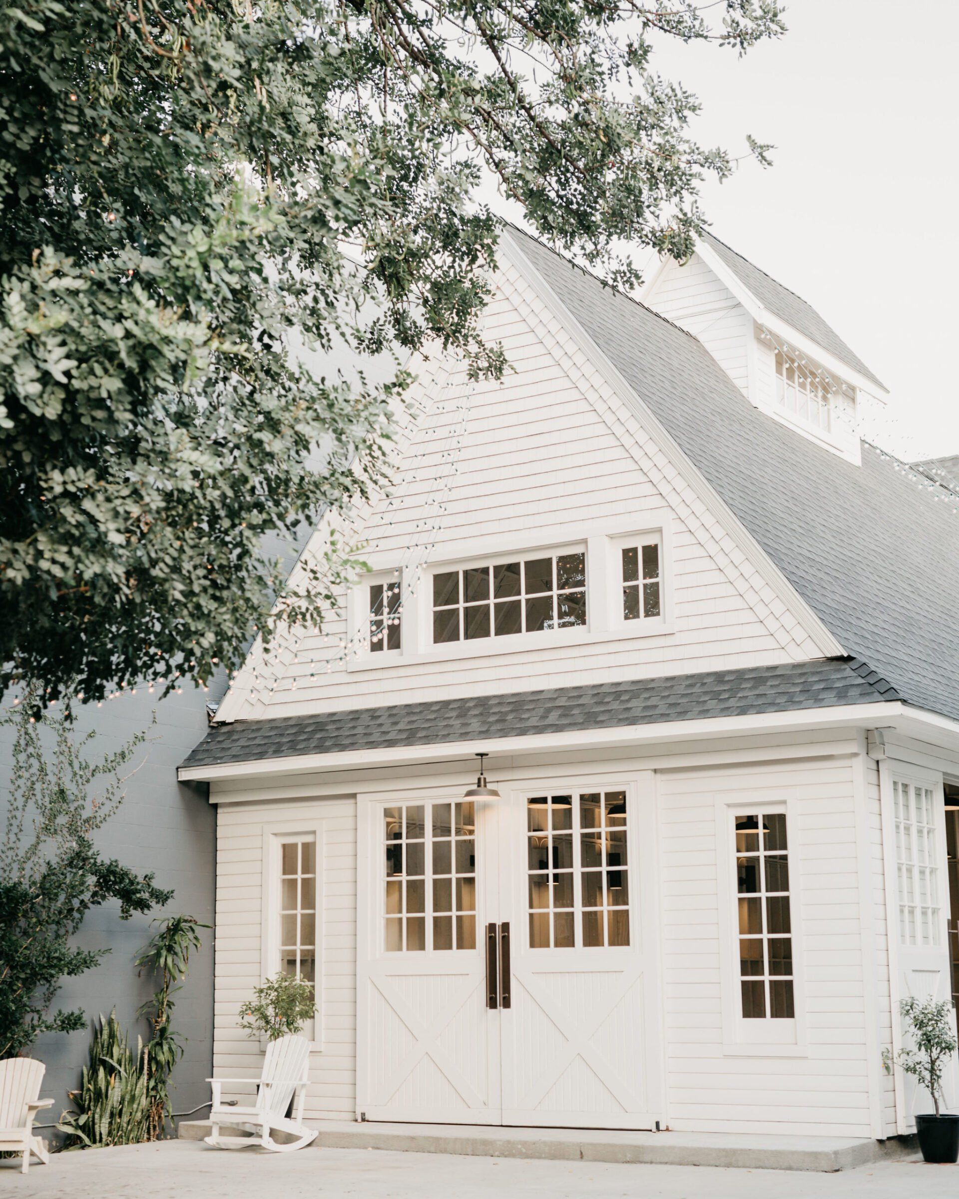 A white house with a black roof is surrounded by trees.