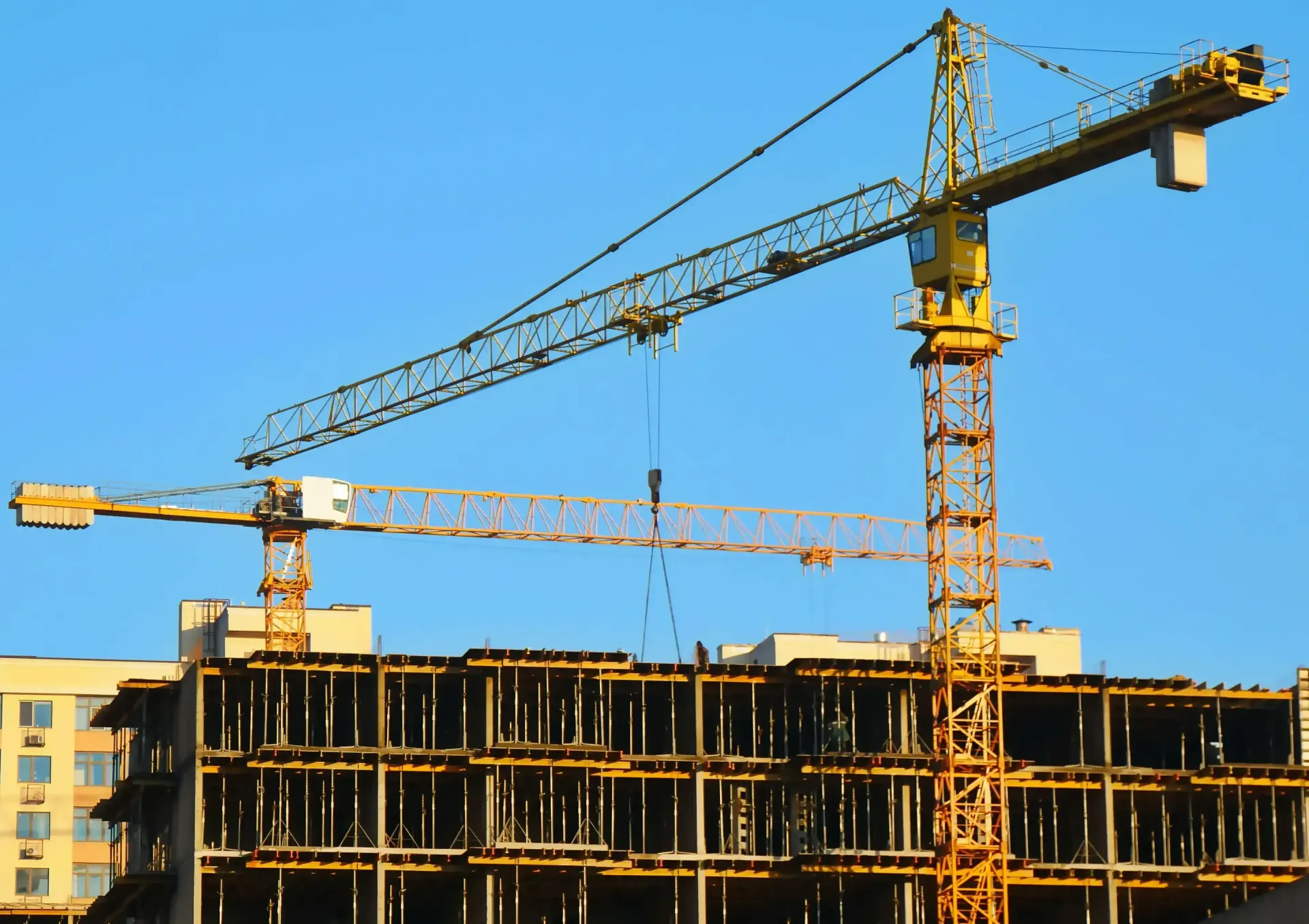 Two yellow construction cranes over a building under construction against a blue sky.