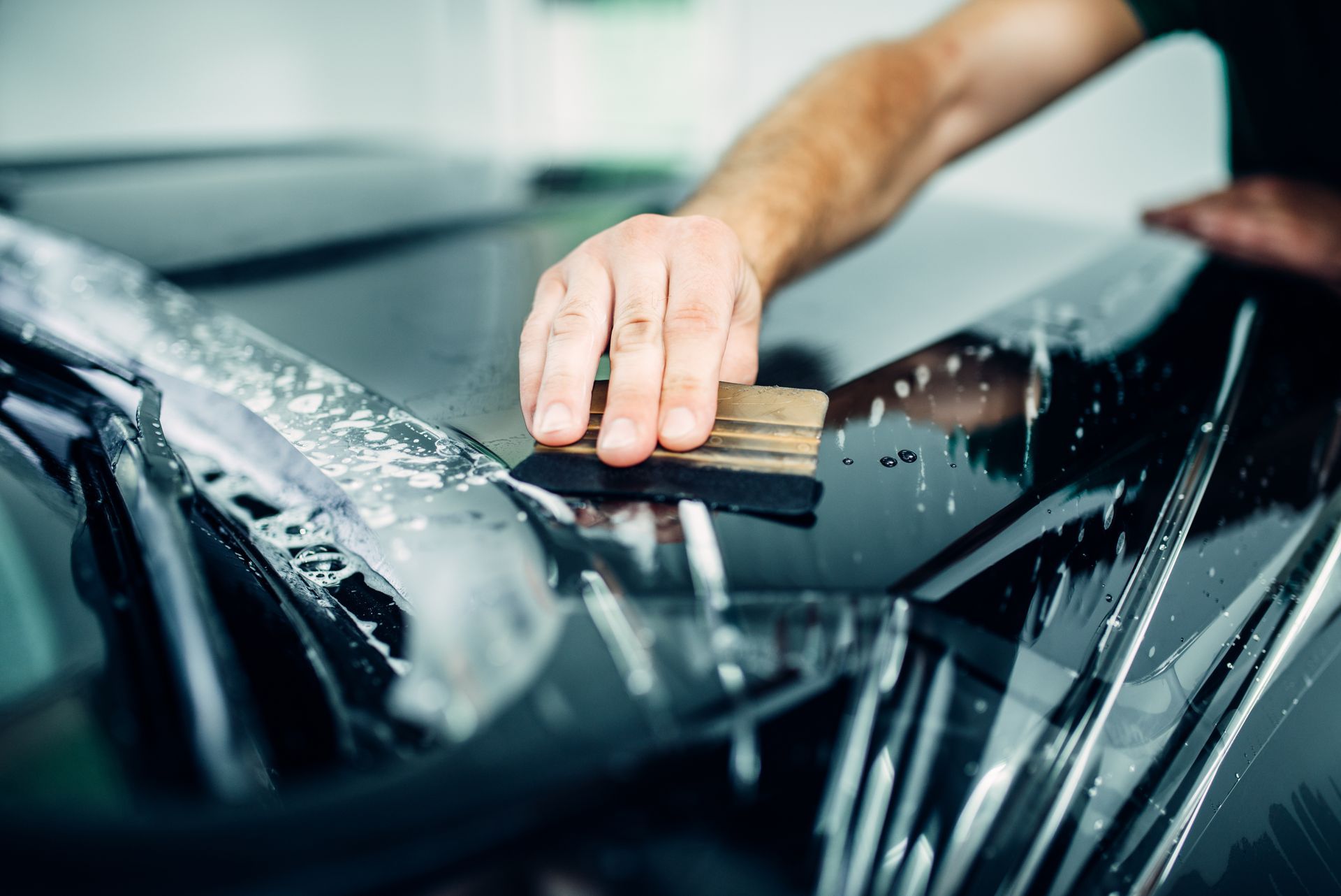 A man is applying a protective film to the hood of a car.