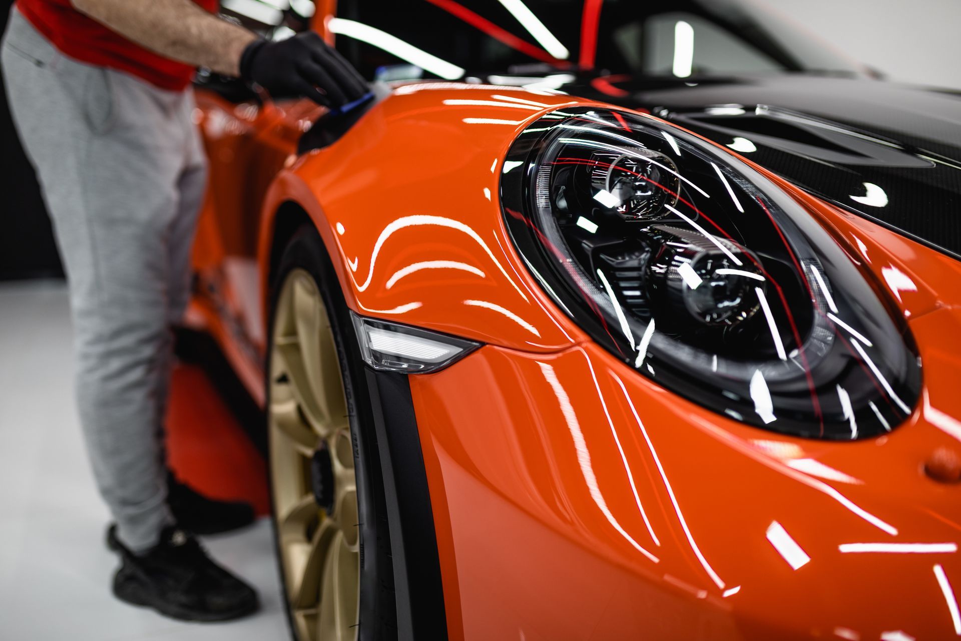 A man is polishing the hood of an orange sports car.