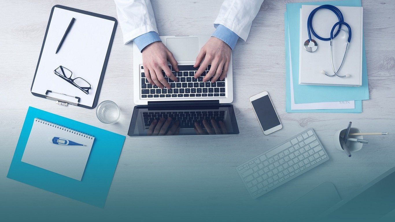 A doctor is typing on a laptop computer at a desk.