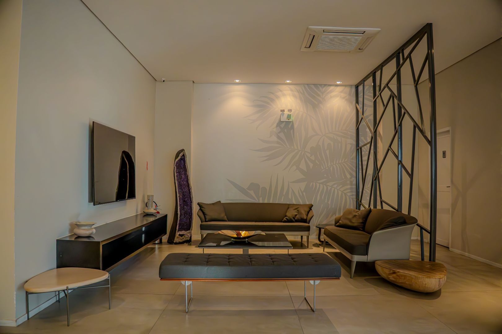 Sala de estar moderna com dois sofás, TV, decoração e divisória geométrica.