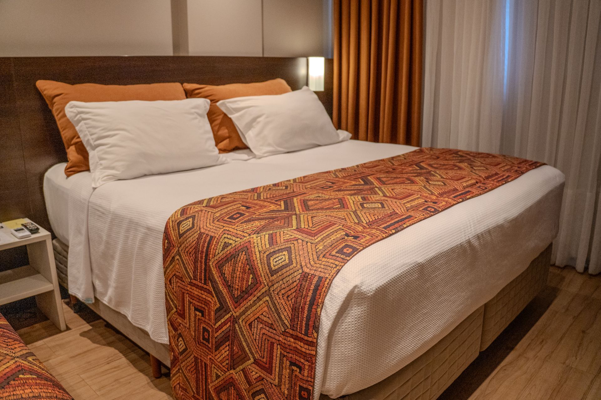 Quarto de hotel com duas camas, uma escrivaninha e uma TV; cores neutras.