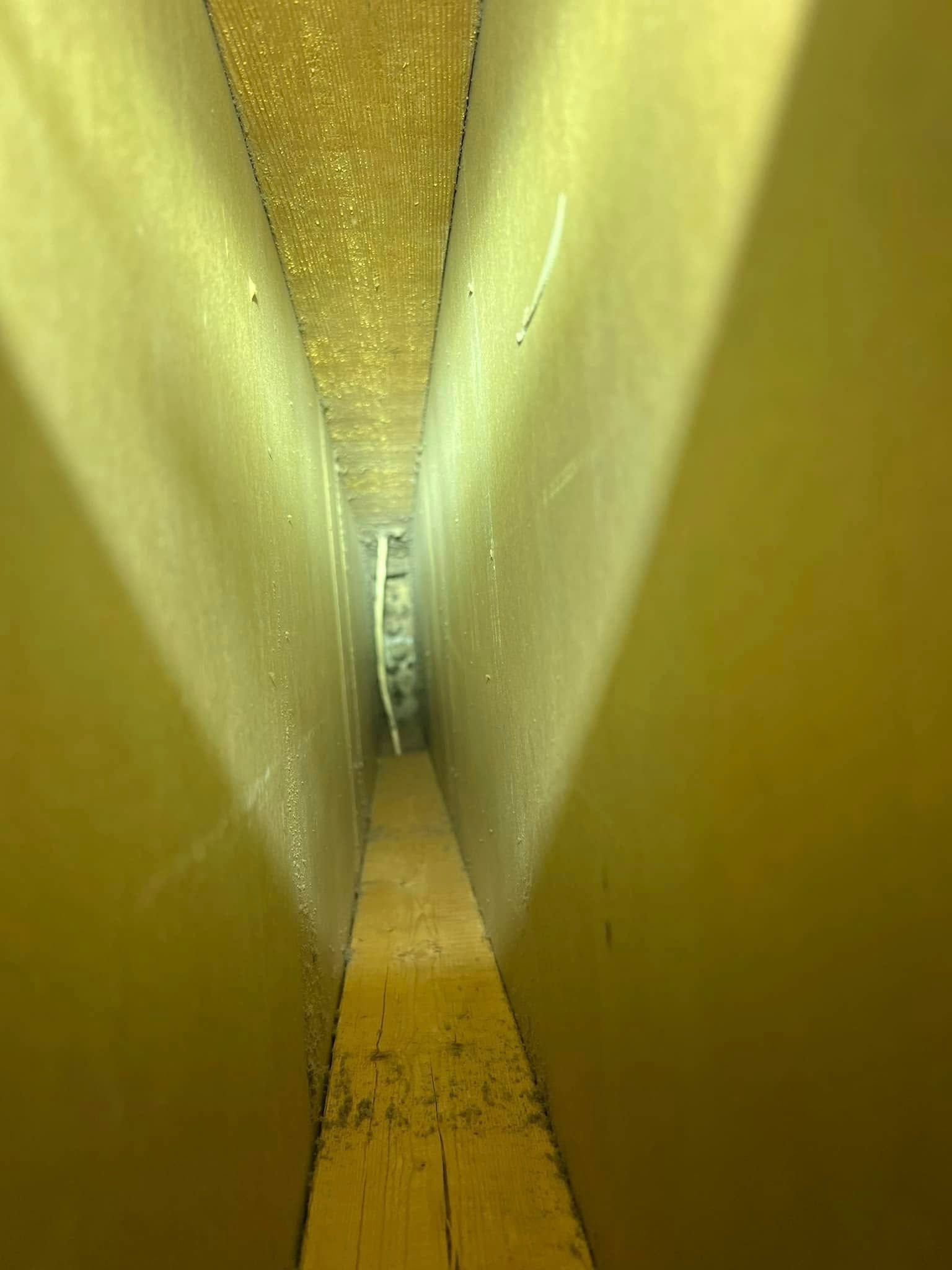 Narrow yellow corridor with white walls and a small round window at the far end.