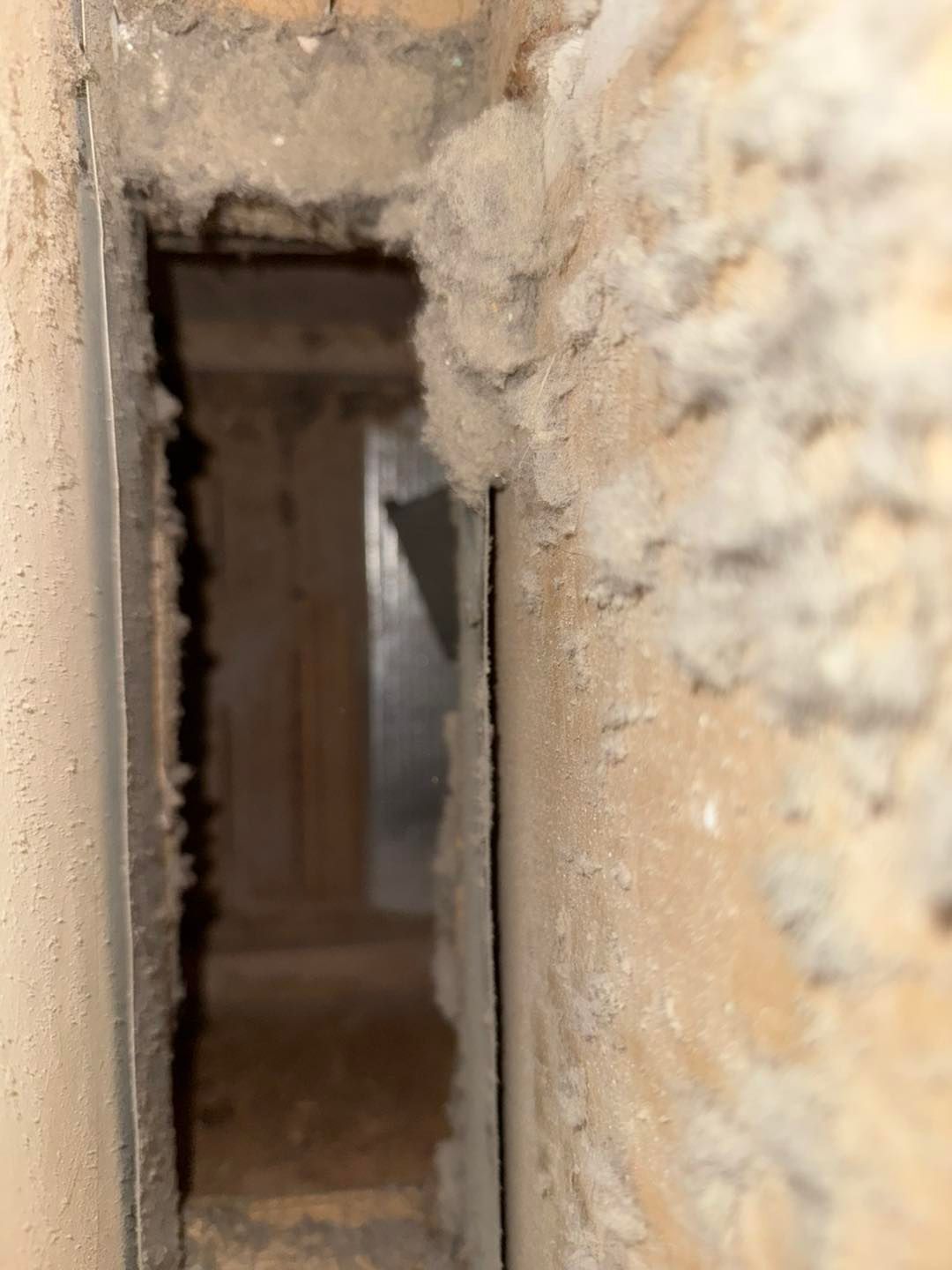 View through a narrow rectangular hole in a dusty beige wall into a dim hallway