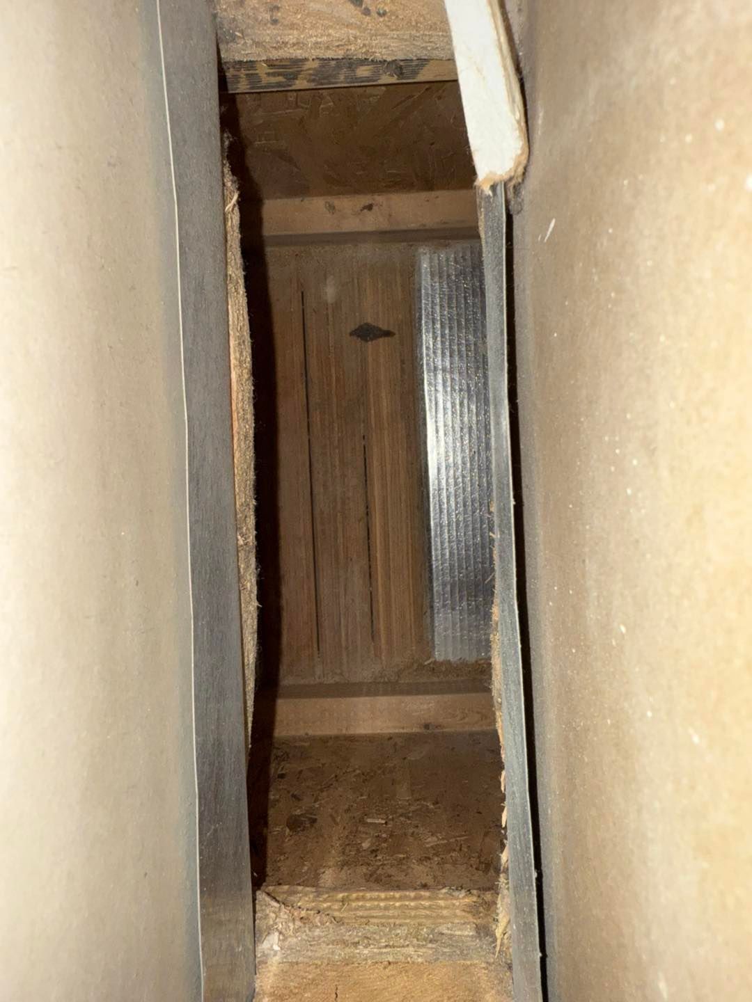 Narrow vertical opening between beige walls, showing a wooden floor below with a metal strip on one side