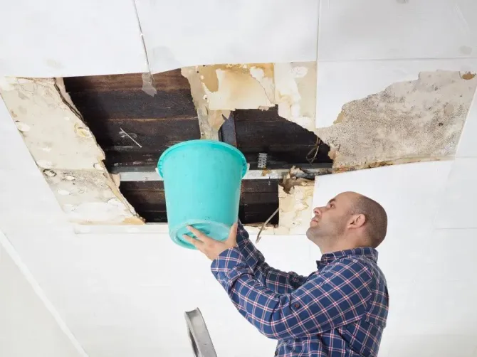 Man catching water from a leaking ceiling with a bucket.