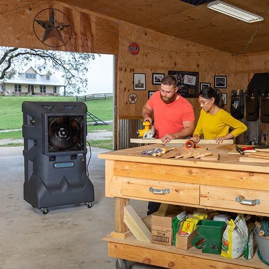 A man and a woman are working on a wooden table in a garage