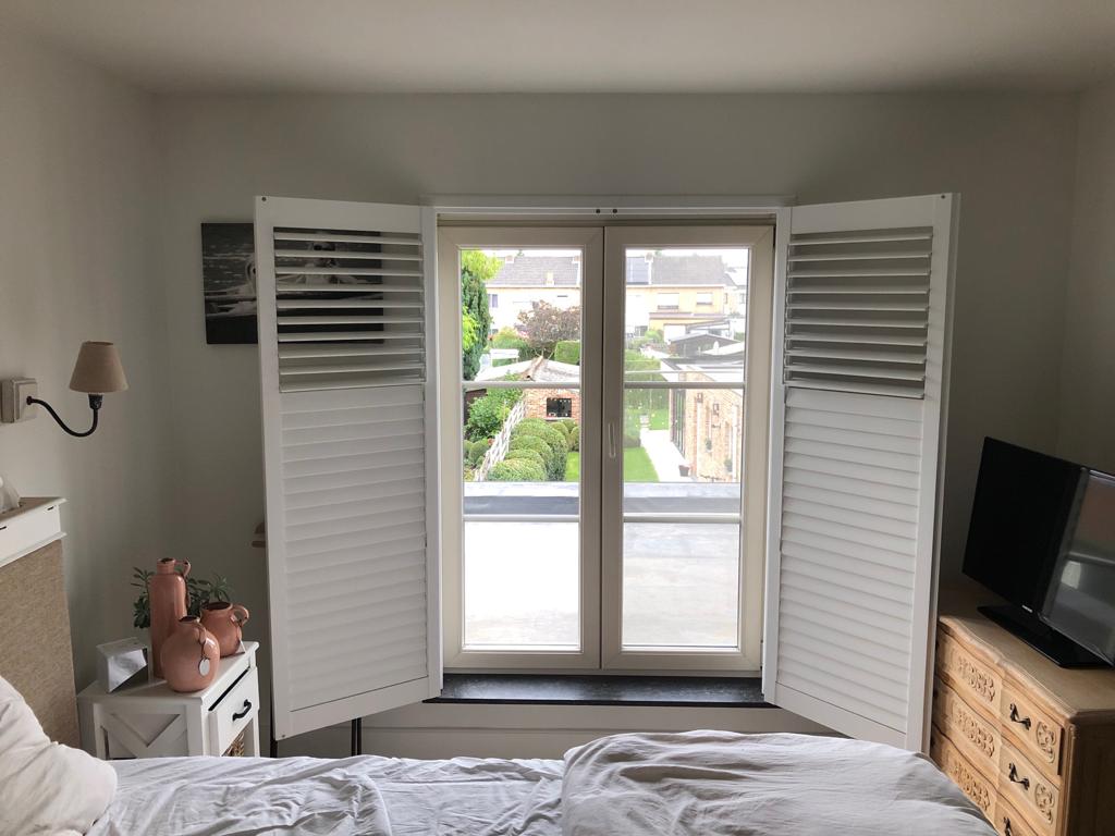 Een slaapkamer met een bed en een raam met open luiken.