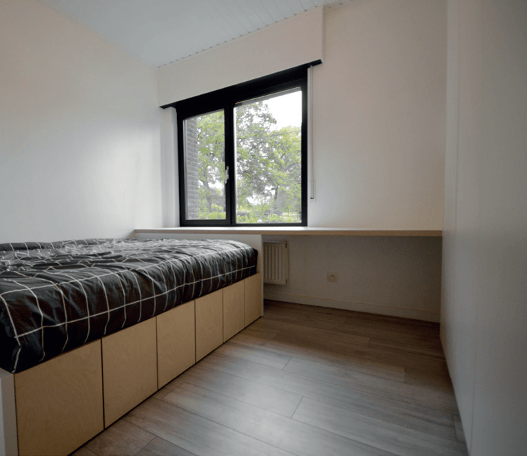 Een kleine slaapkamer met een bed en een raam.