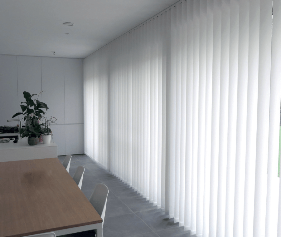 Een eetkamer met een tafel en stoelen en witte verticale jaloezieën voor de ramen.
