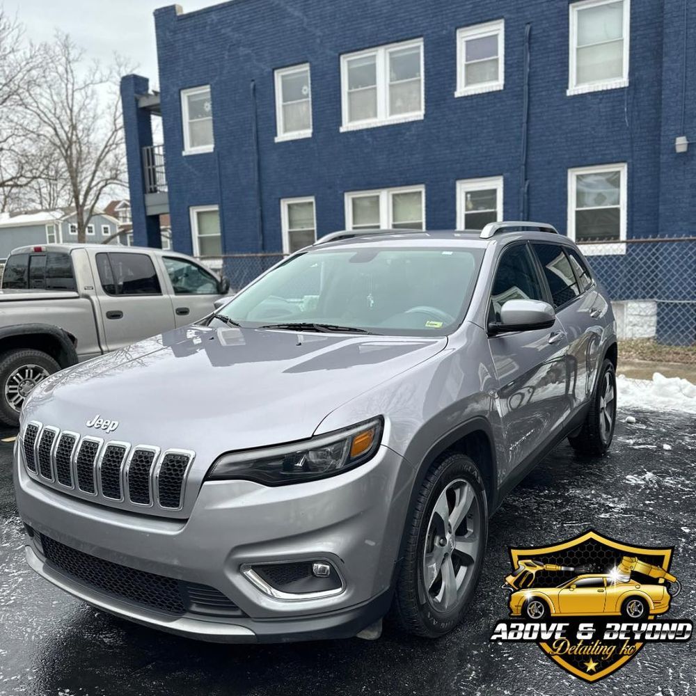 Silver Jeep Cherokee parked in front of a blue building; business logo in the corner.