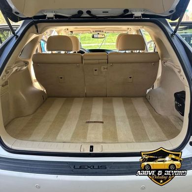 Clean, tan-carpeted trunk of a white Lexus SUV; backseats up, outdoors.