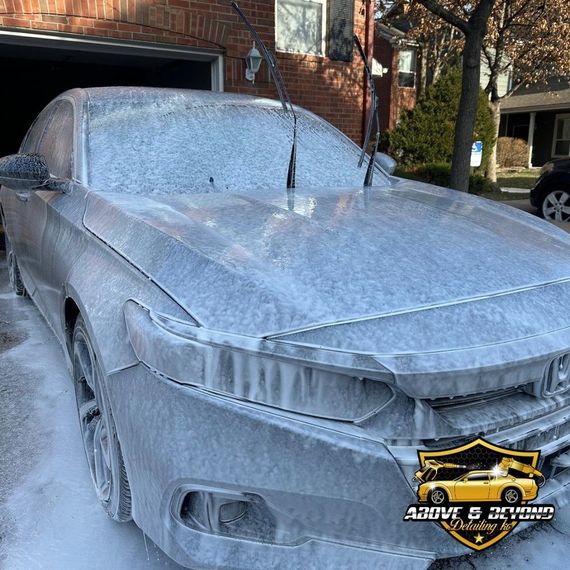 Car covered in foam suds during a car wash in a driveway.