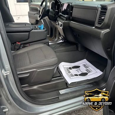 Gray truck interior with black seats and floor mats, and a paper with footprints.
