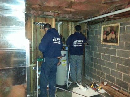 Two plumbers in blue hoodies installing a water heater in a basement.