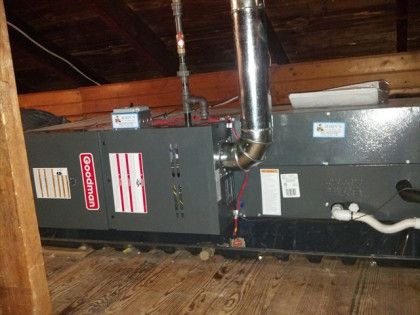 Goodman furnace in an attic with ductwork and gas line.