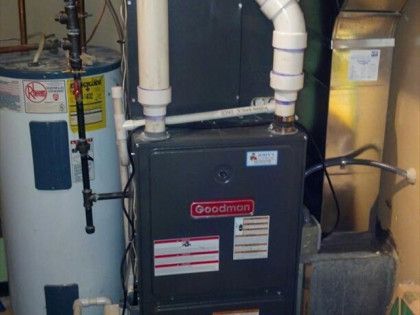 Furnace next to a water heater in a utility room. Goodman brand furnace with PVC pipes.