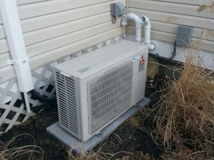 Mitsubishi heat pump unit on concrete slab, mounted on siding with pipes.