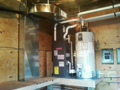 Water heater and electric tank side-by-side in a utility room; metal ductwork and wooden shelves.