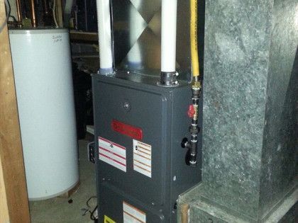 Furnace and hot water tank in a basement. Grey furnace with two white exhaust pipes.