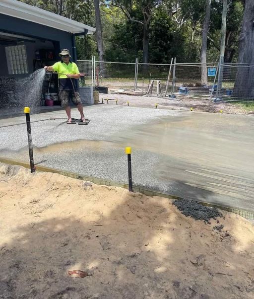 A Man Is Watering A Concrete Driveway In Front Of A House— Tuncote Concrete Constructions in Medowie, NSW