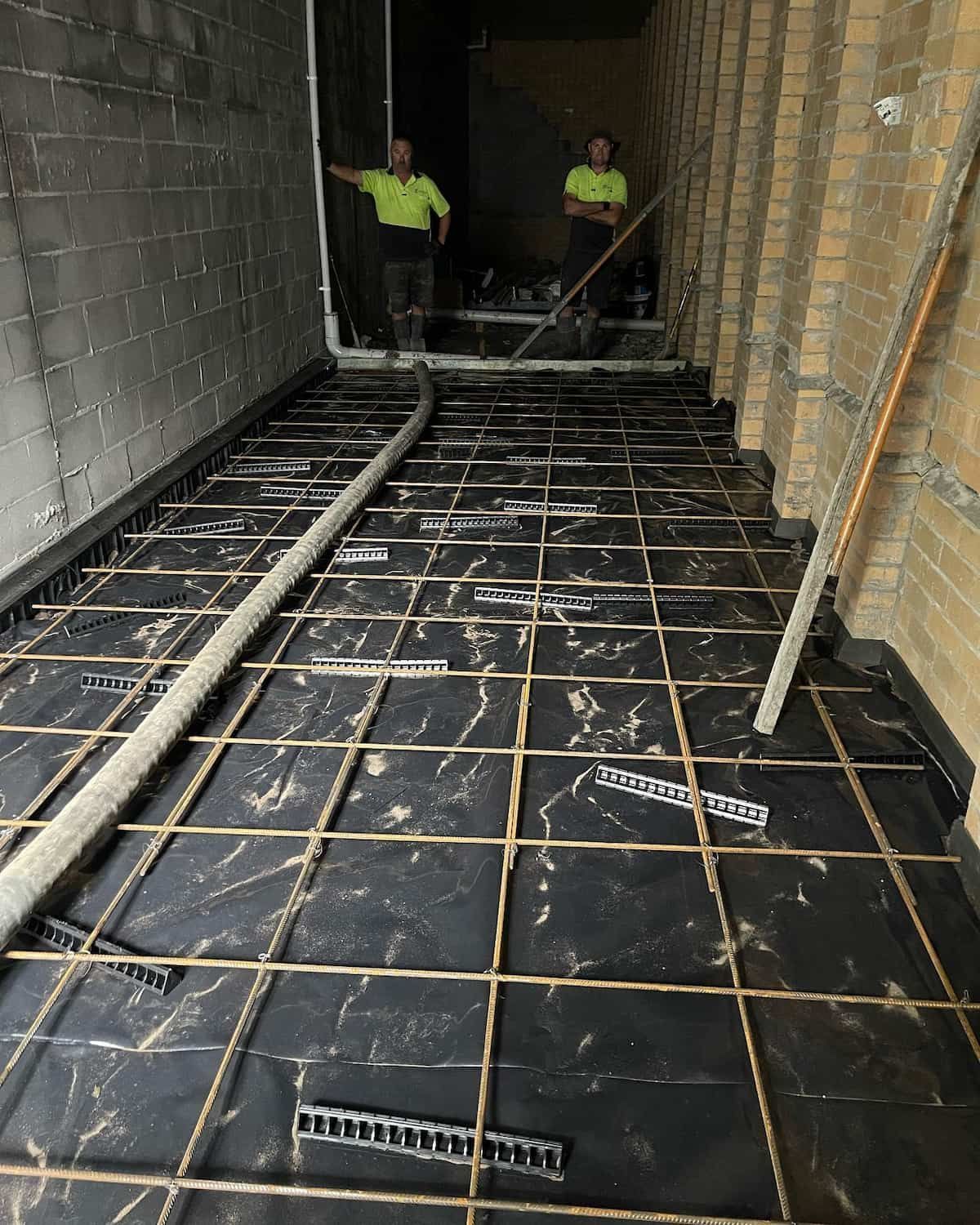 Two Men Are Working On A Concrete Floor In A Building — Tuncote Concrete Constructions in Raymond Terrace, NSW