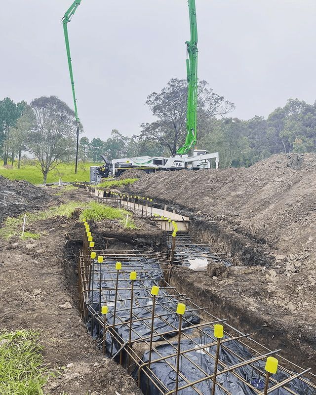 A Green Concrete Pump Is Being Used To Pour Concrete Into A Trench — Tuncote Concrete Constructions in Anna Bay, NSW